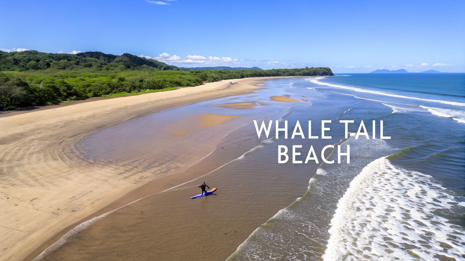 Aerial view of Whale Tail Beach, Costa Rica, with a person paddleboarding along the sandy shore.