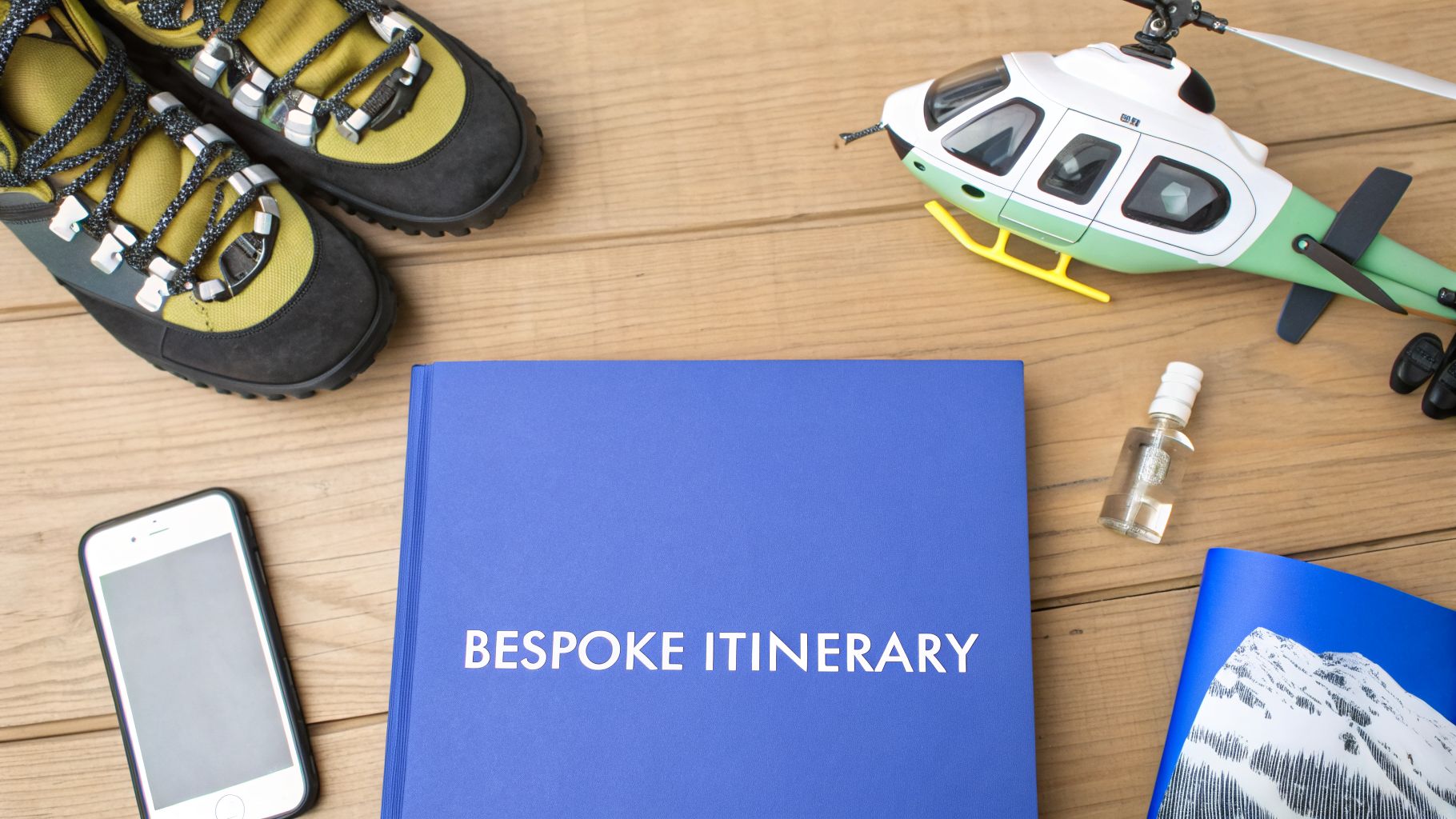 Travel planning flatlay with 'Bespoke Itinerary' book, boots, helicopter, and phone for a luxury ski resort.