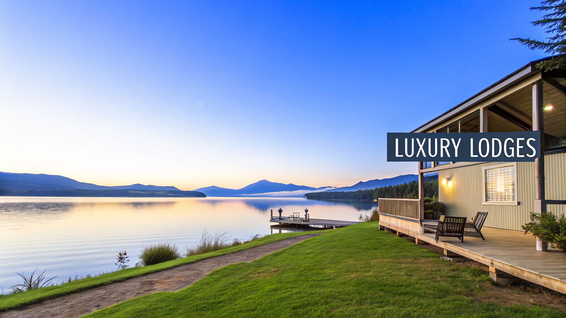 A luxurious waterfront lodge with a deck, a pier, and mountains reflecting on a calm lake at dawn.