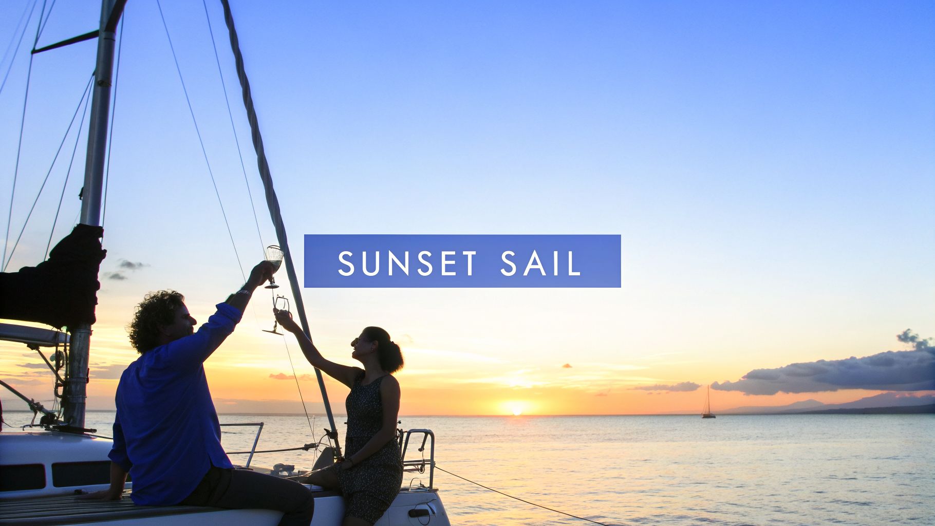 A happy couple enjoys a romantic sunset sail on a boat, toasting with wine glasses.