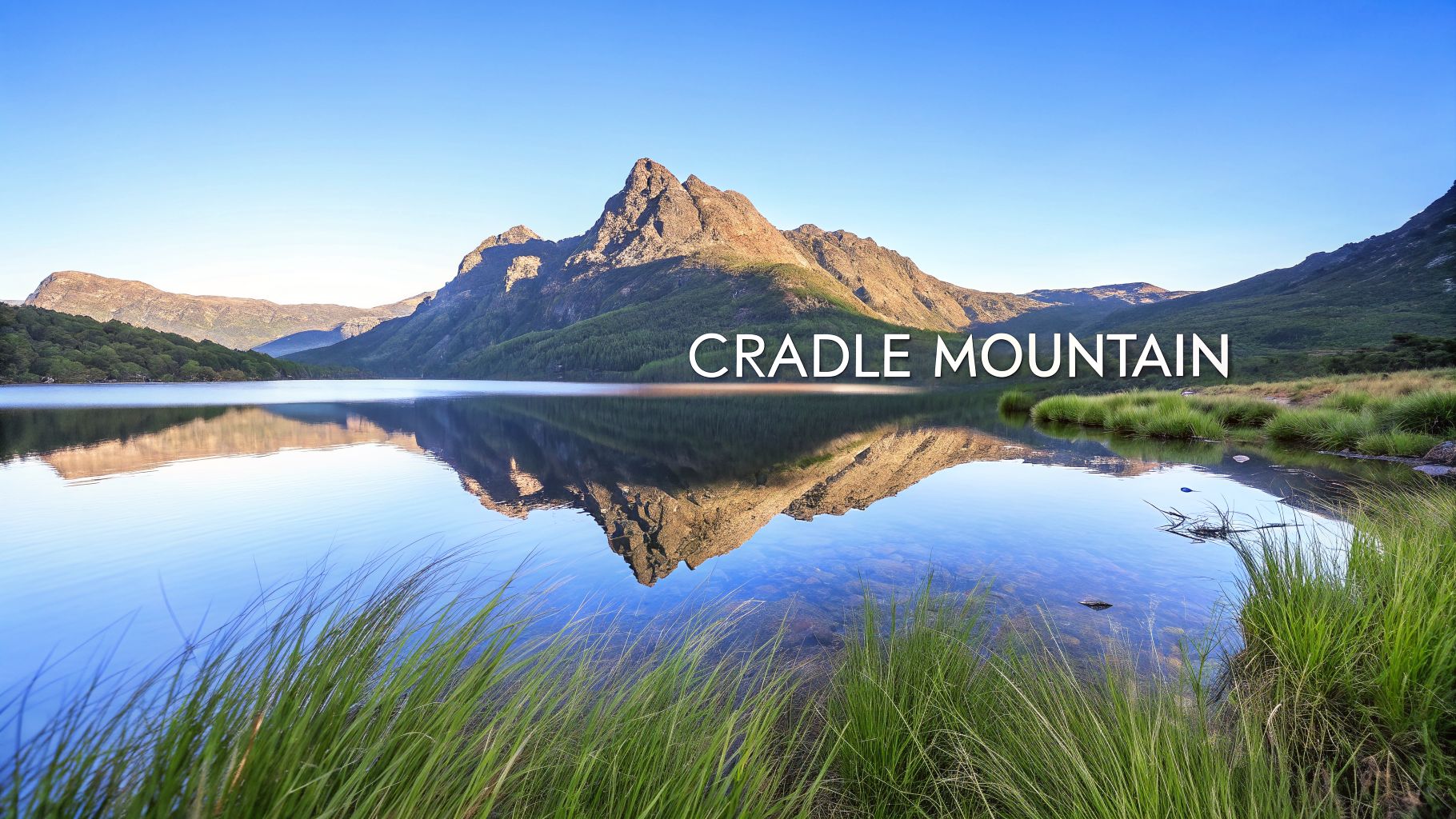 A majestic view of Cradle Mountain reflecting in a serene lake with vibrant green grass.