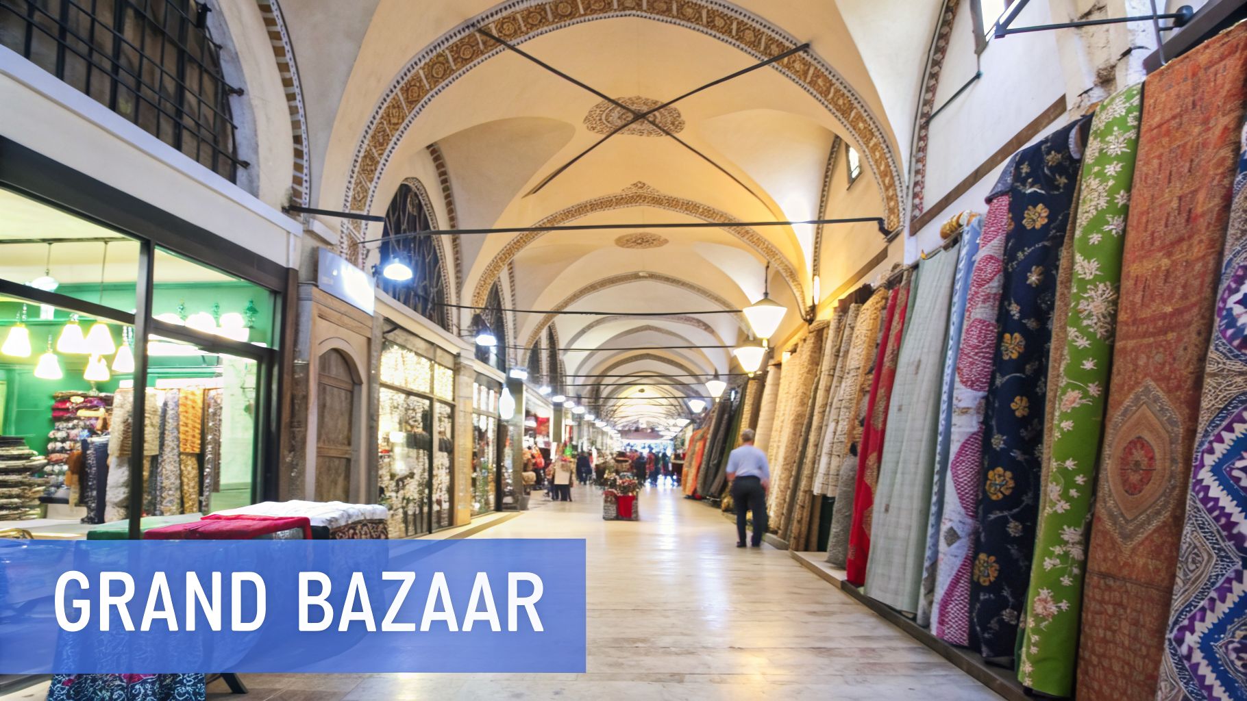 Inside the historic Grand Bazaar in Istanbul, showing a bustling arched corridor with colorful shops and textiles.