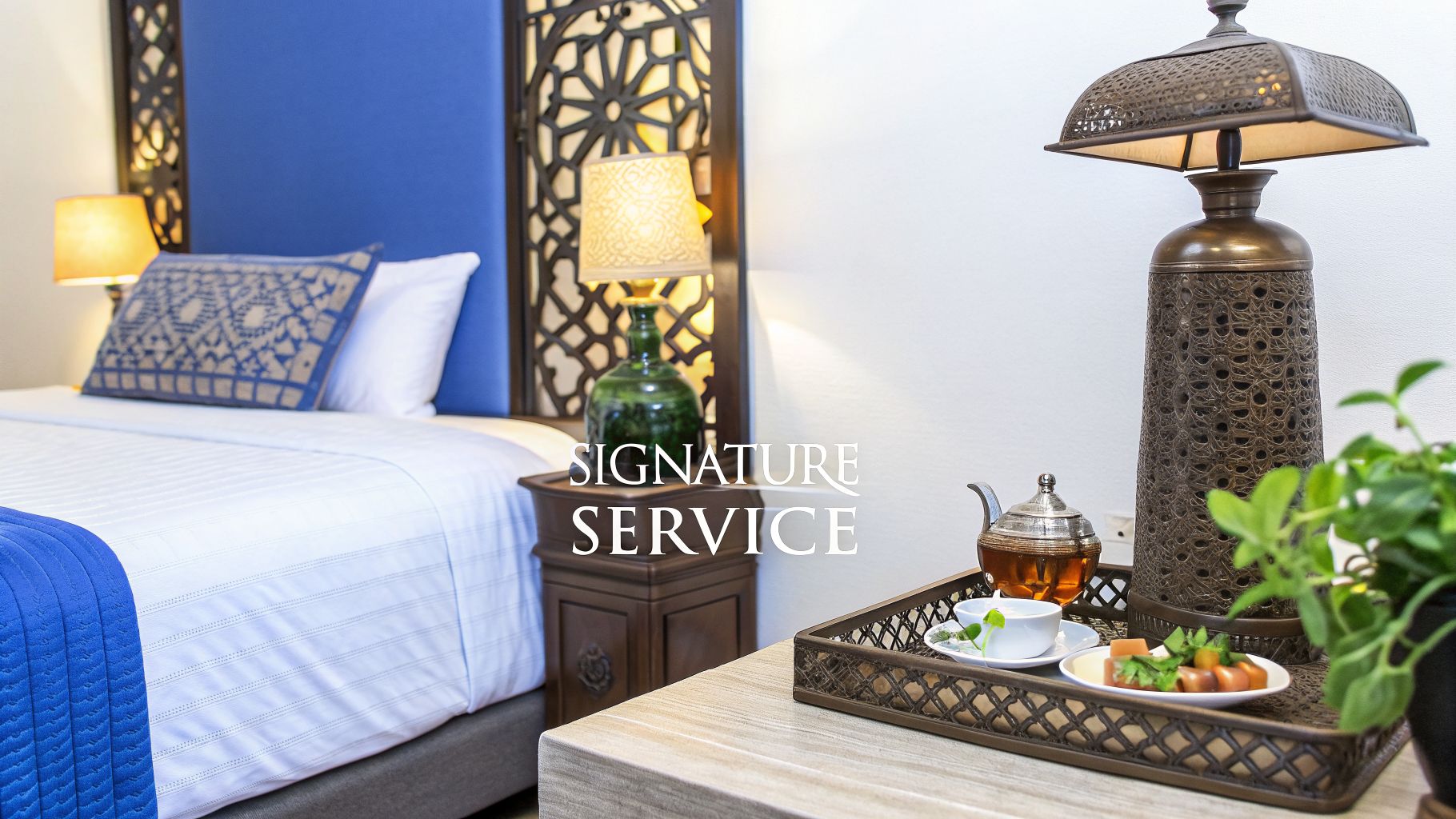 A luxurious hotel room with a neatly made bed, a side table, and a tray with tea and snacks.