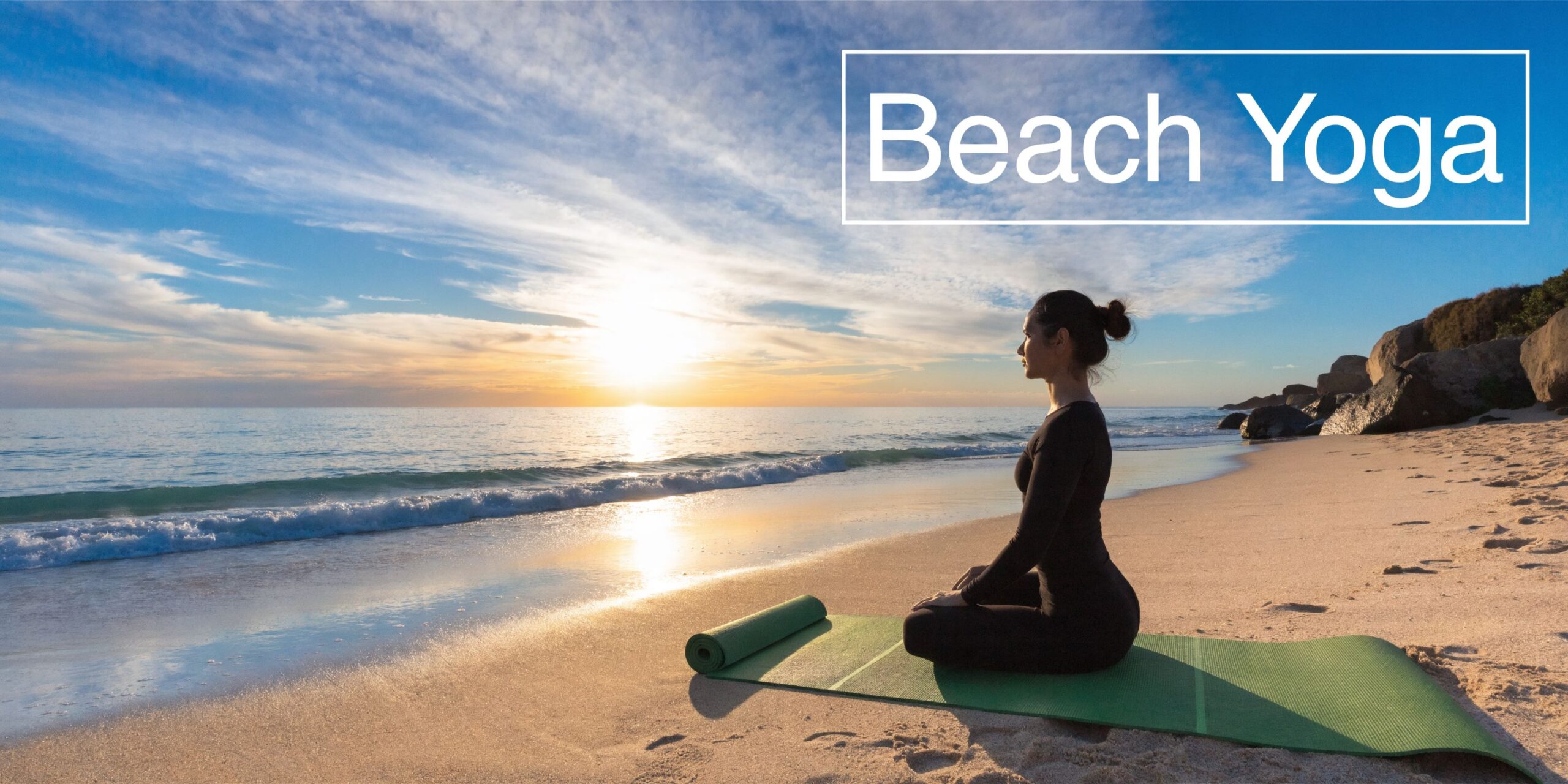 A woman meditating on a green yoga mat on a sandy beach during a beautiful sunset