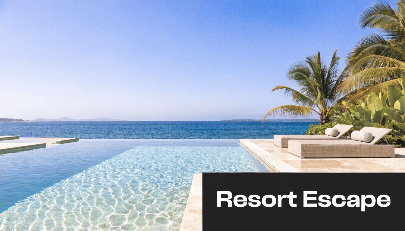Luxurious infinity pool overlooking a calm ocean with palm trees and sun loungers on a wooden deck.