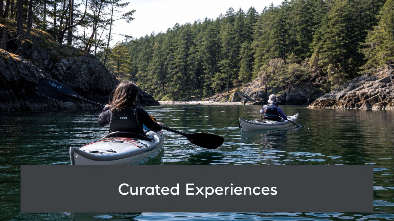 Two people kayaking on a calm waterway surrounded by lush green forests and rocky shorelines.