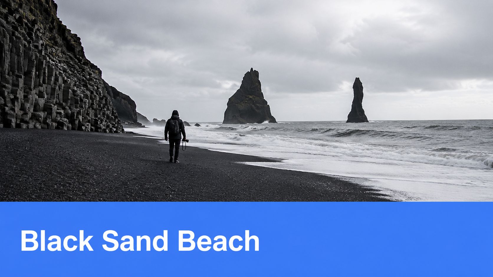 A photographer walking along the iconic black sand beach in Iceland with basalt rock formations in background